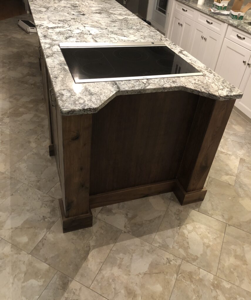 Close-up view of a modern kitchen island featuring a granite countertop and an integrated cooktop, surrounded by tiled flooring.