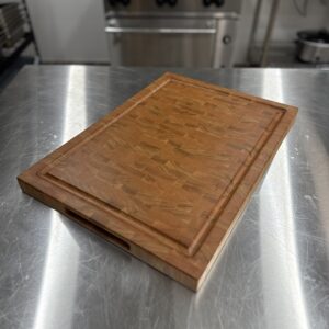 Angled view of cherry end grain cutting board showing grain pattern, juice groove and finger wells.