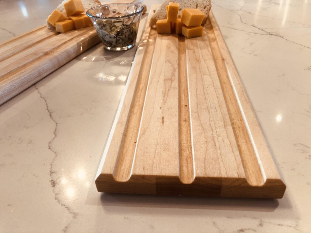 Close-up of a handcrafted wooden cutting board featuring neatly arranged cheese cubes and bread, placed on a marble countertop.