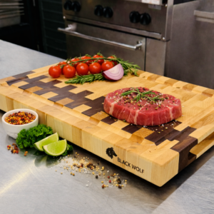 Eastern Maple end‑grain cutting board with Walnut accent by Black Wolf Industries, displayed in a professional kitchen with fresh ingredients and a seasoned steak on top.
